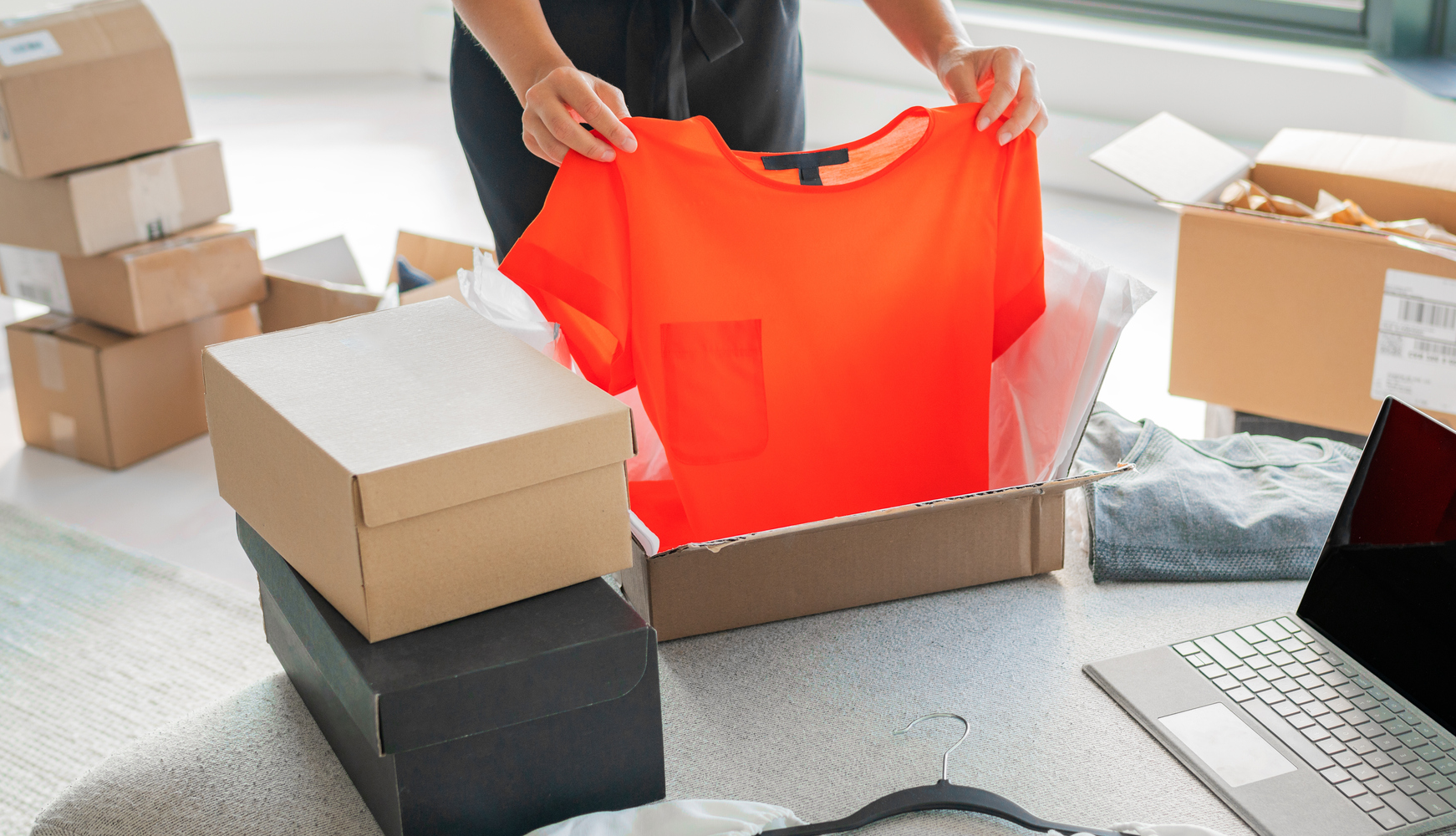 A female seller who is packaging an orange t-shirt in a box to complete the shipment process