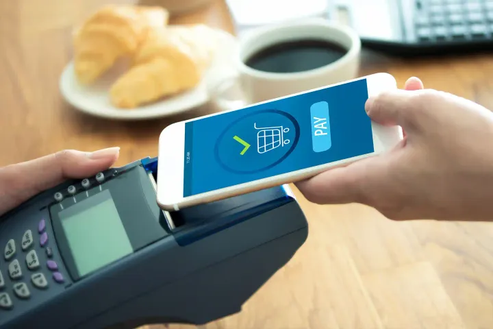 A customer using a mobile payment system on their smartphone to tap an RFID reader at the point of sale